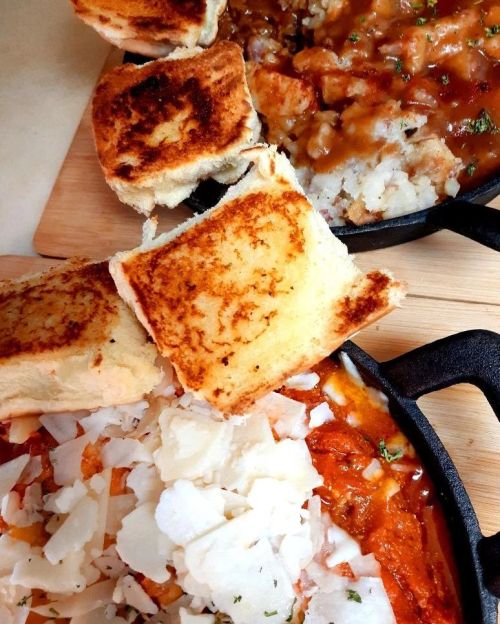 A close-up of two cast iron skillets with toasted bread and a savory dish topped with cheese and herbs.