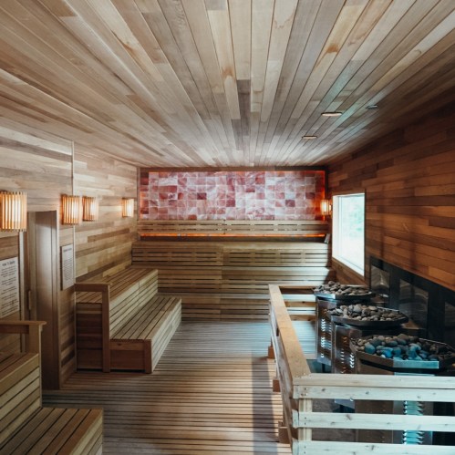 A serene wooden sauna interior with benches, soft lighting, and a stone heater, creating a relaxing atmosphere.
