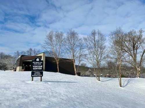 A visitor center building surrounded by snow and bare trees under a cloudy sky.