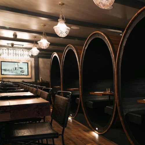 Cozy restaurant interior featuring wooden barrel booths, elegant lighting, and wooden tables.