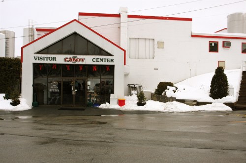 A snowy scene featuring the Cabot Visitor Center with a red-trimmed roof and holiday decorations.