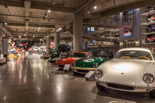 A spacious museum interior showcasing vintage cars and motorcycles, with various models on display under bright lights.