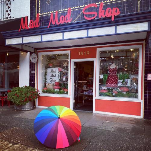 A colorful rainbow umbrella sits in front of the Mad Mod Shop, featuring a vibrant storefront and decorative window displays.