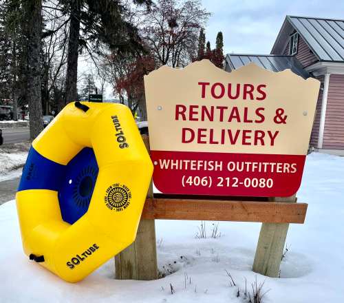 A colorful yellow and blue inflatable tube next to a sign for Whitefish Outfitters offering tours, rentals, and delivery.