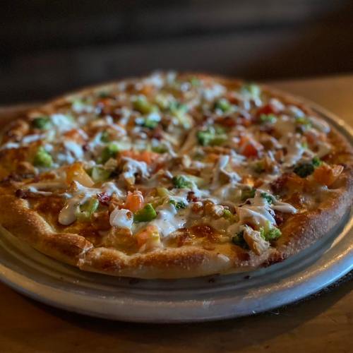 A freshly baked pizza topped with vegetables and drizzled with sauce, served on a round plate.