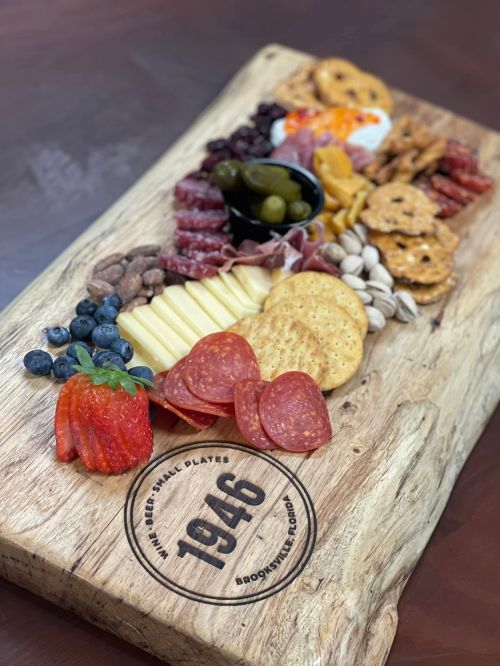 A wooden platter filled with assorted meats, cheeses, fruits, nuts, and pretzels, elegantly arranged for sharing.