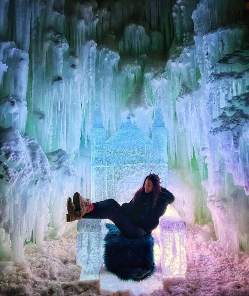 A person sits on an ice throne surrounded by colorful ice formations in a winter wonderland.