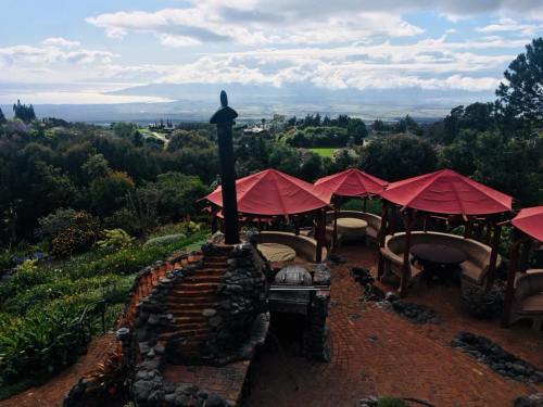 Scenic view of a garden restaurant with red umbrellas, stone grill, and lush greenery overlooking a distant landscape.