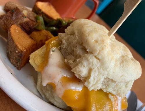 A biscuit sandwich with melted cheese and a side of roasted potatoes and greens on a plate.