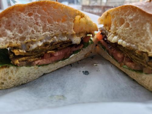 A close-up of a sandwich cut in half, featuring layers of lettuce, tomato, and a crispy fried filling on soft bread.
