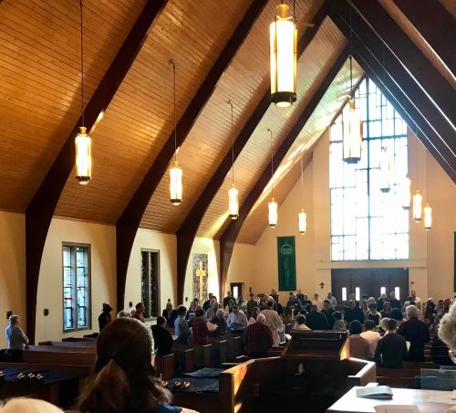 A large group of people gathered inside a church with high wooden ceilings and stained glass windows.