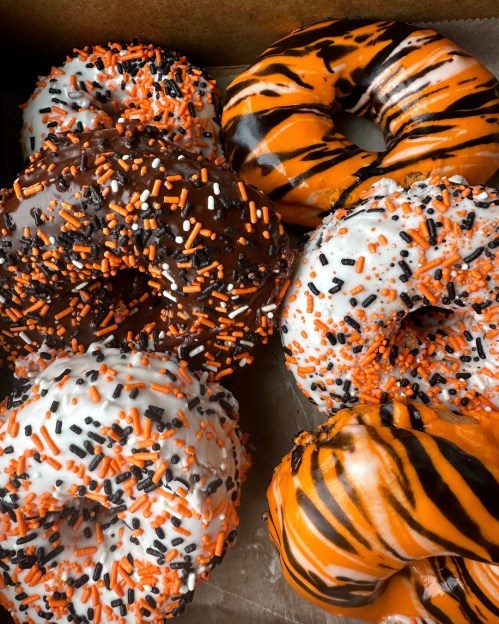 A box of festive donuts decorated with orange, black, and white icing and sprinkles, featuring a tiger stripe design.