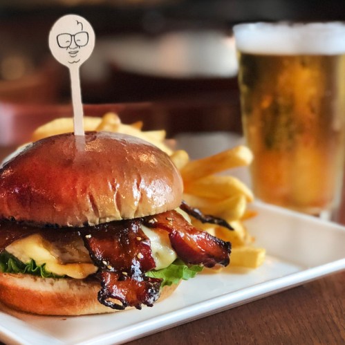 A delicious burger with bacon, cheese, and lettuce, served with fries and a glass of beer in the background.