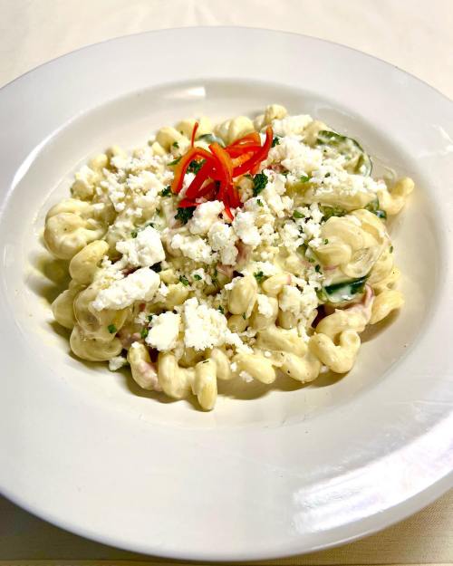 Creamy pasta dish topped with crumbled feta, herbs, and red pepper slices, served in a white bowl.