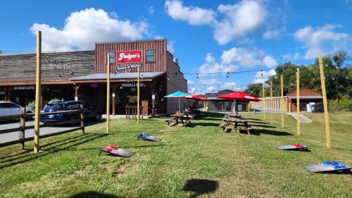 Outdoor seating area with picnic tables and umbrellas, alongside a rustic building under a blue sky with clouds.