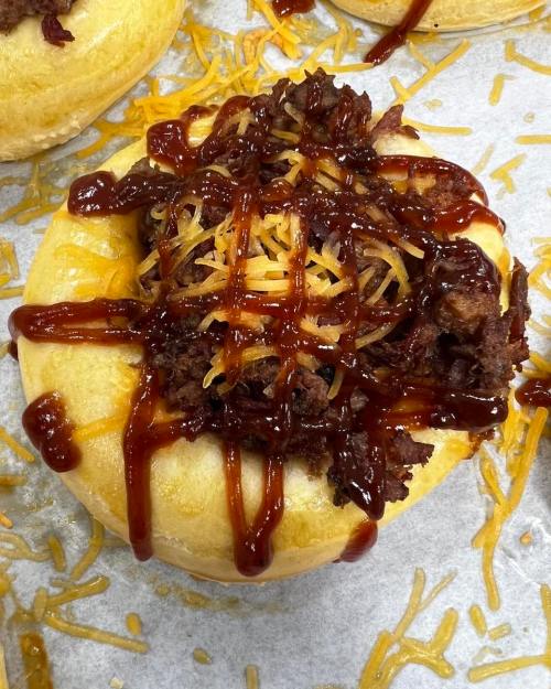 A close-up of a savory dish featuring a bread bowl filled with meat, cheese, and drizzled with barbecue sauce.