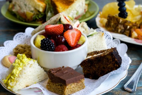 A plate of assorted desserts and fruit, including cake, cookies, and a bowl of mixed berries and sliced fruit.