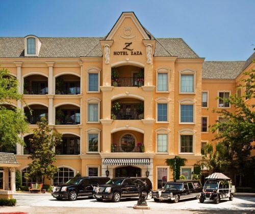 Exterior view of Hotel Zaza featuring a tan building, balconies, and several black luxury cars parked in front.