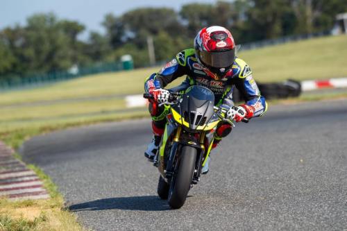 A motorcyclist in racing gear leans into a turn on a track, showcasing speed and skill.