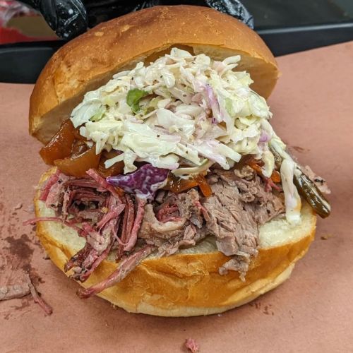 A close-up of a sandwich filled with pulled beef, coleslaw, and barbecue sauce on a toasted bun.