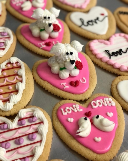 Colorful heart-shaped cookies decorated with icing, featuring a dog, roses, and romantic messages.