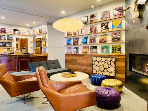 Cozy lounge with vinyl records on the wall, modern furniture, a fireplace, and colorful poufs.