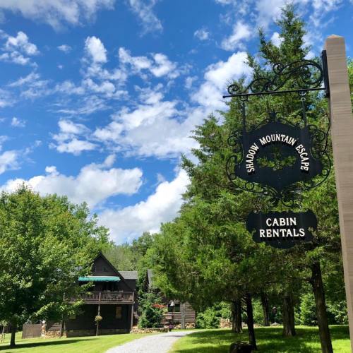 Sign for "Shadow Mountain Escape" cabin rentals, with a scenic view of trees and a blue sky in the background.