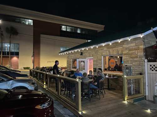 A lively outdoor dining area at night, with patrons seated at a wooden deck outside a restaurant.