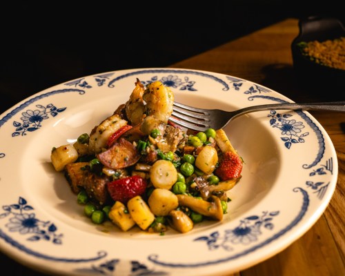 A plate of sautéed shrimp and vegetables, including peas and radishes, garnished with herbs on a decorative dish.
