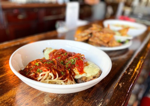 A bowl of spaghetti topped with marinara sauce and cheese, with a side of crispy appetizers in the background.