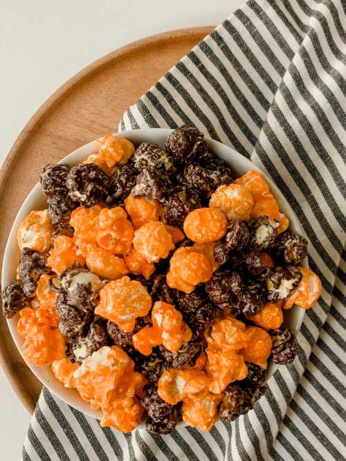 A bowl of orange and chocolate popcorn on a wooden plate, with a striped cloth beside it.