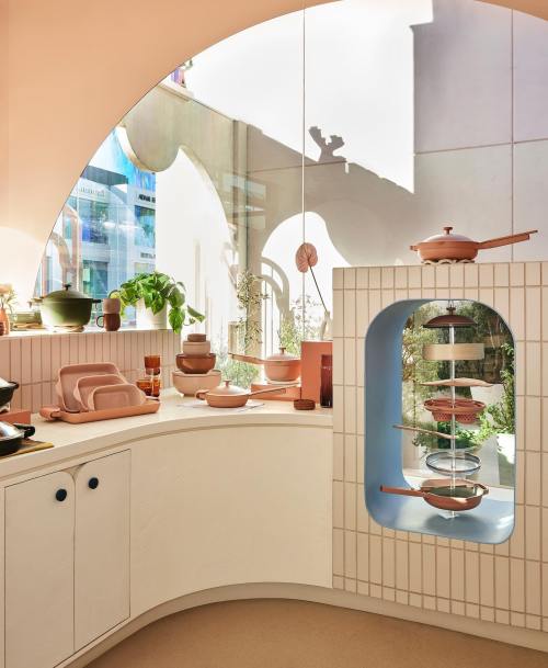 A modern kitchen with pastel-colored cookware and dishes, featuring curved architecture and natural light.