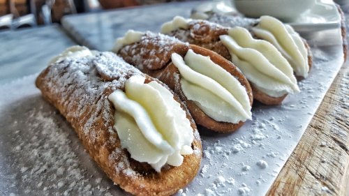 Three cream-filled pastries dusted with powdered sugar, arranged on a white plate.