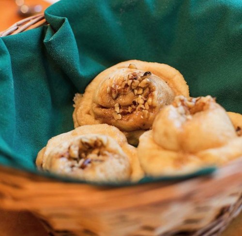 A basket lined with green fabric holds three sweet rolls topped with chopped nuts.