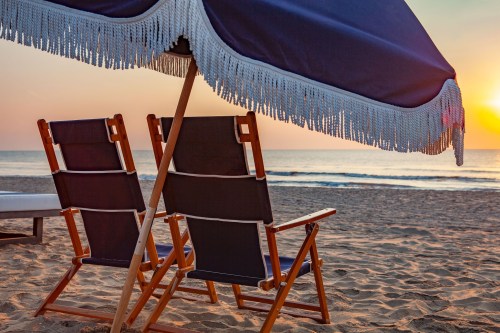 Two beach chairs under a fringed umbrella, facing a serene sunset over the ocean.