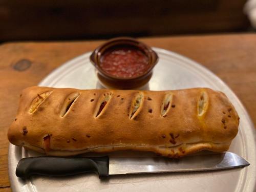 A golden-brown calzone with slits on top, served on a plate with a side of marinara sauce and a knife.