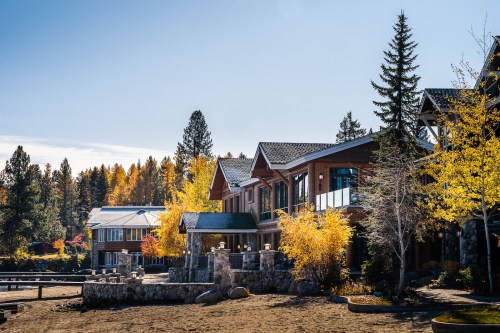 A lakeside view of modern cabins surrounded by autumn trees and clear blue skies.