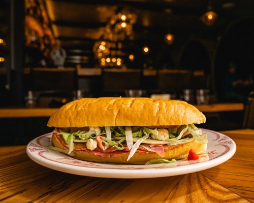 A close-up of a sandwich on a plate, filled with lettuce, meats, and served in a cozy, dimly lit restaurant.
