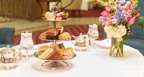 A tiered stand with assorted pastries and sandwiches, accompanied by glasses of water and a floral centerpiece.