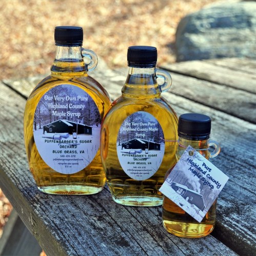 Three bottles of Highland County maple syrup on a wooden table, featuring labels with the brand name and location.