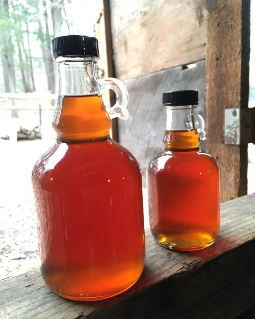 Two glass bottles filled with amber-colored liquid, sitting on a wooden surface in a rustic setting.