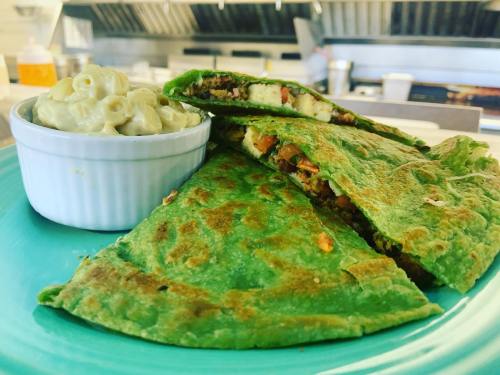 A vibrant green quesadilla filled with ingredients, served with a side of creamy macaroni and cheese in a white bowl.