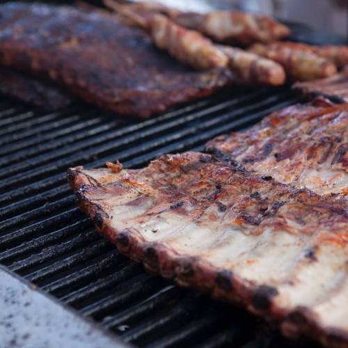 Grilled ribs and skewers cooking on a barbecue grill, showcasing a smoky, charred texture.