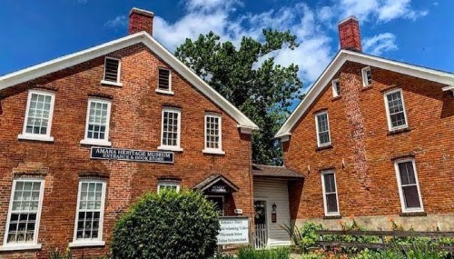 Exterior view of the Amana Heritage Museum, featuring red brick buildings and a blue sky with scattered clouds.