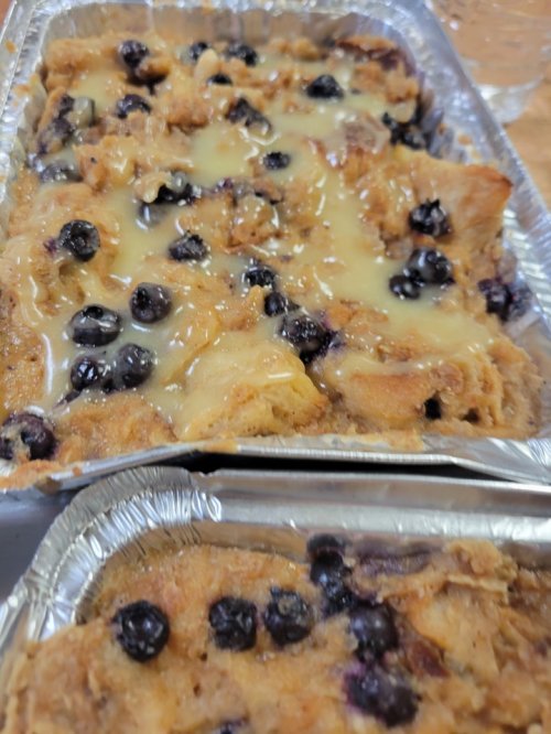 Baked dish with a golden topping, mixed with blueberries, in aluminum trays.