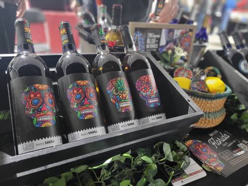 Four bottles of colorful, skull-themed wine labeled "Sangria" displayed in a wooden crate with decorative elements.