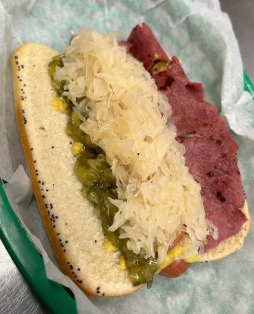 A sandwich on a poppy seed bun filled with layers of corned beef, sauerkraut, and relish.