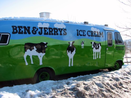 A colorful Ben & Jerry's ice cream truck with cow graphics parked on a snowy landscape.