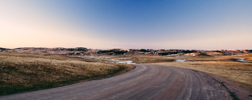 A winding road through a vast, open landscape with rolling hills and a clear sky at dusk.