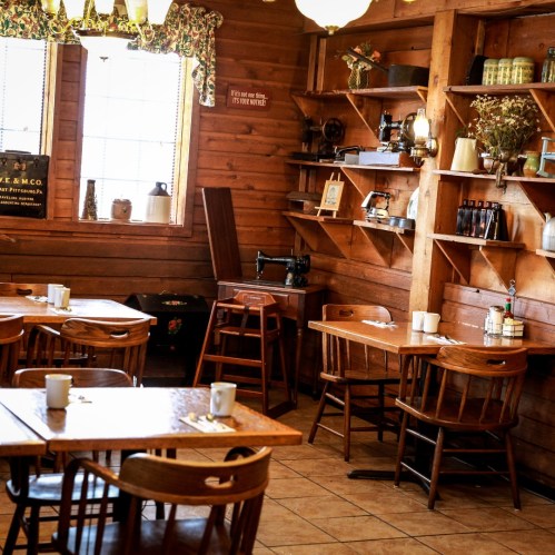 Cozy wooden interior of a café with tables, chairs, and shelves filled with vintage items and decor.